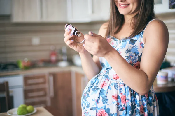 Cropped view of medicine in hands of smiling pregnant woman standing in kitchen