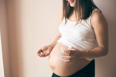 Evde duran ve su ile vitaminler alarak büyük göbek ile hamile kadın görünümünü kırpılmış