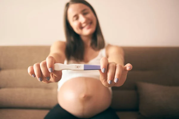 Selective focus of pregnancy test in hands of smiling woman in white shirt