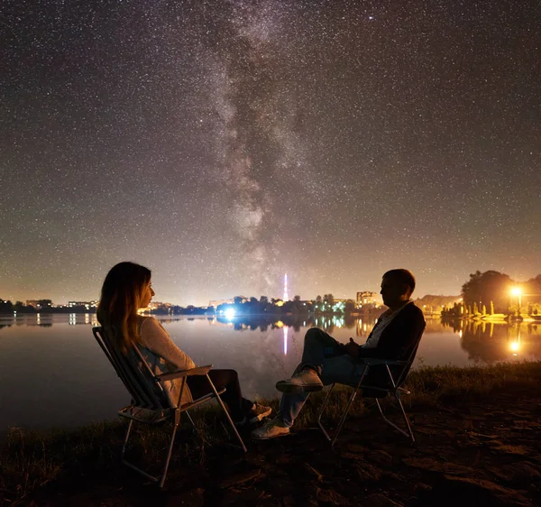 Couple tourists resting near tent and campfire under sky full of stars and Milky way