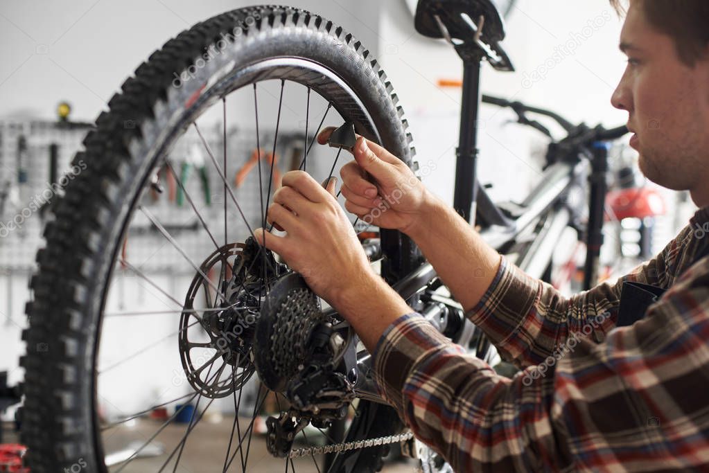male mechanic working in bicycle repair shop, repairman fixing bike using special tool, wearing protective work wear