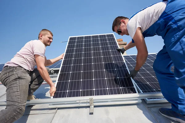 現代の家の屋根の上の青い太陽電池モジュールを持ち上げる電気技師 — ストック写真