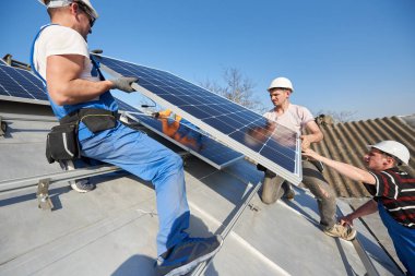 Electricians lifting blue solar module on roof of modern house. Alternative renewable energy ecological concept. clipart