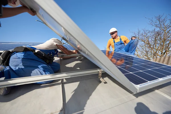 現代の家の屋根の上の青い太陽電池モジュールを持ち上げる電気技師 — ストック写真