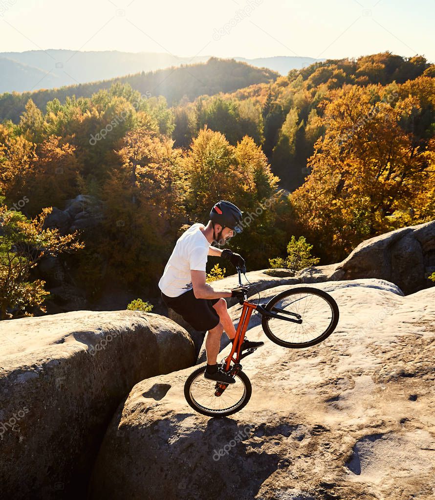 Young male cyclist balancing on trial bicycle on top of big boulder