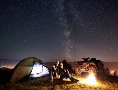 Mutlu çift erkek ve kadın trevelers oturma yakınındaki turistik çadır ve kamp ateşi yakma
