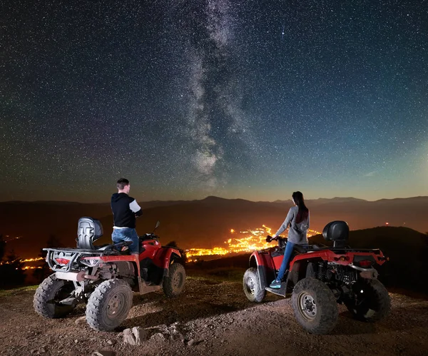 couple of man and woman tourists standing on atv quad motorbikes on top of mountain