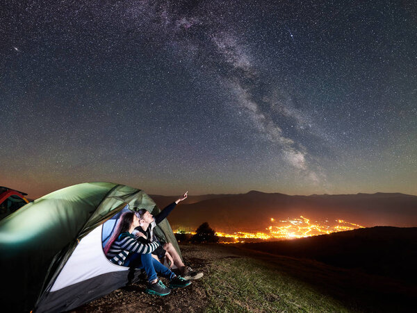 Young happy couple hikers resting at camp in illuminated tourist tent