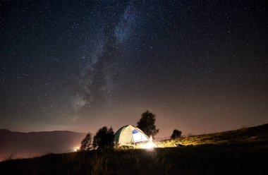 Işıklı çadır ve kamp ateşi altında büyülü gece gökyüzü yıldız ve Samanyolu dolu