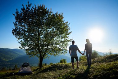 Arkadan güneşli sabah kamp ve büyük ağaç dağlarda yakın dinlenme iki mutlu genç erkek ve kadın yürüyüşçü görünüşü