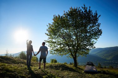 Arkadan güneşli sabah kamp ve büyük ağaç dağlarda yakın dinlenme iki mutlu genç erkek ve kadın yürüyüşçü görünüşü