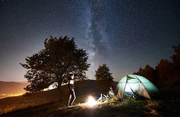 愉快的情侣徒步者在发光的旅游帐篷附近的营火中休息 — 图库照片