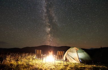 Parlayan çadır, iki sandalye ve şenlik ateşi altında inanılmaz güzel gece gökyüzünde yıldızlar ve Samanyolu dolu