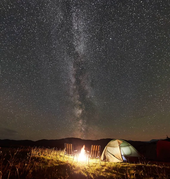 Tourist camping in mountains near big tree at nighttime