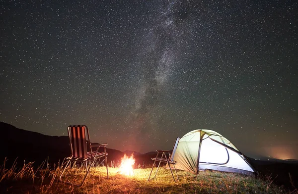 Tourist camping in mountains near big tree at nighttime