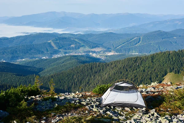 Summer camping on top of mountain with foggy valley, pine trees and distant mountains on background