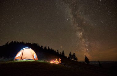 Birlikte yanında aydınlatmalı turist çadır kamp ateşi etrafında oturan arkadaşlar yürüyüşçü
