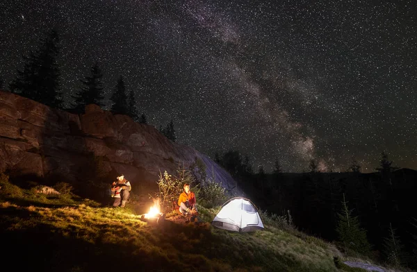 Romantic couple hikers resting together while sitting beside campfire