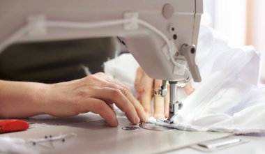 İşyerinde profesyonel üretim makinesinde beyaz kumaş dikiş eller, yakın çekim
