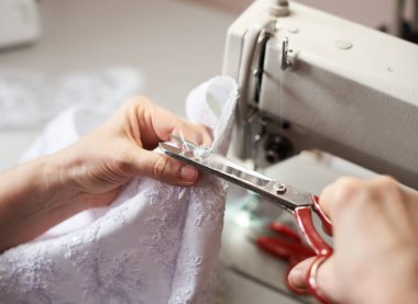 Close up view of tailor using scissors for cutting off edge of fabric in sewing process clipart