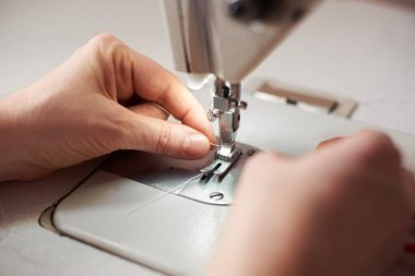Close up of tailor skillful fingers pulling thread in needles loop on modern manufacturing machine  clipart