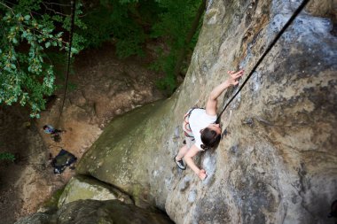 Genç bayan kaya tırmanışçısı iple kayalıklara tırmanıyor.