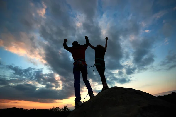 Silhouettes of young couple climbers standing on the rock and holding hands