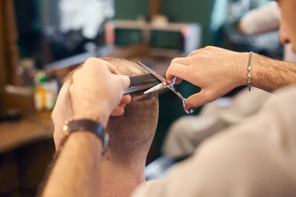 close up of barber hands using of scissors and comb during short male haircut