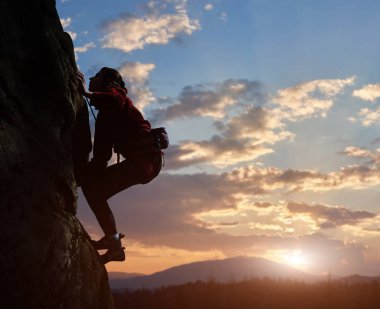 Young woman climbing high up on rock at sunset in mountains