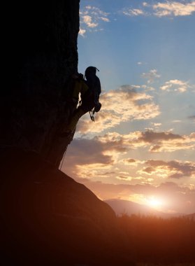 Bulutlu gün batımı arka plan üzerinde doğal kayalık duvara tırmanma erkek siluet yan görünümü 