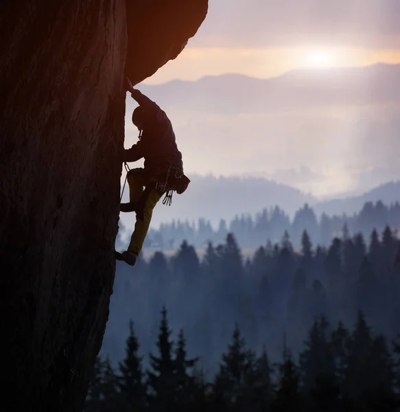 Silhouette of man rock climbing on straight vertical rock on sunrise background