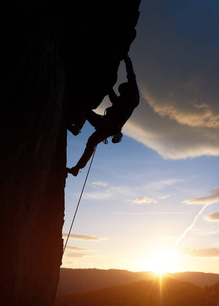Silhouette of sport man climbing up to top of mountain summit during sunset