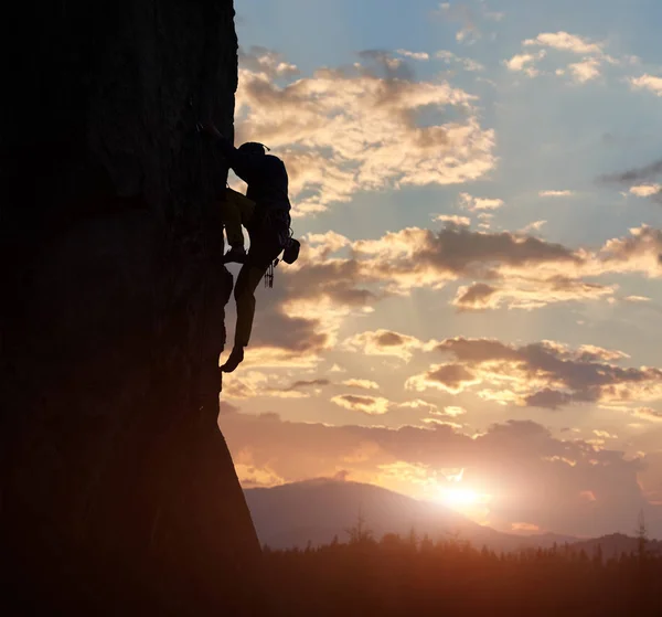 Side view of male silhouette climbing on natural rocky wall on cloudy sunset background