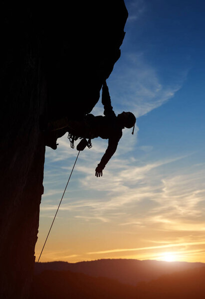 Silhouette of sport man climbing up to top of mountain summit during sunset