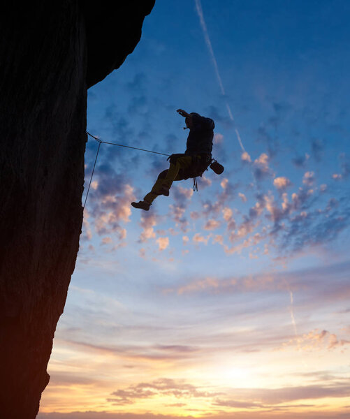 Скалолазный силуэт, спускающийся с вершины сложного скального маршрута
