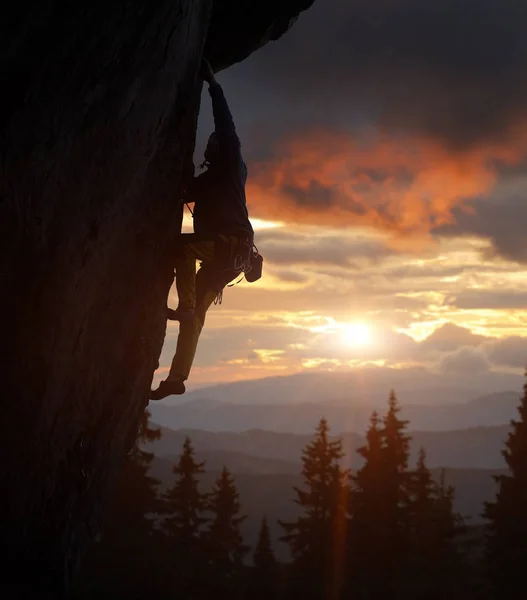 明るい太陽を照じながら急な崖の上で行動する登山家男性のシルエットの側面図 — ストック写真