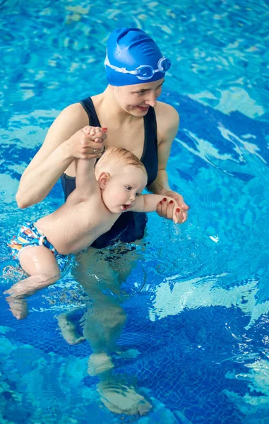 Young mother and her small infant boy at baby swimming lesson doing various exercises in water