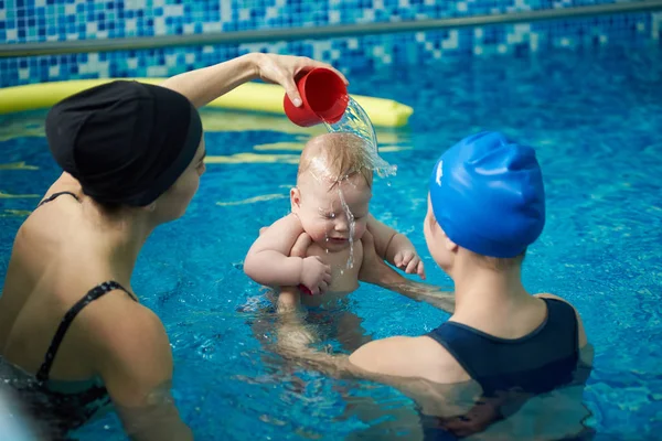 Baby in swimming pool and two women in swimming cap