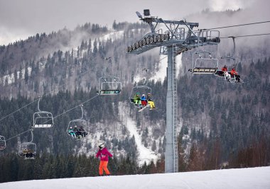 Bukovel, Ukrayna - 09 Aralık 2018: Kayakçılar ve snowboardcular, Karpatlar 'ın sisli, gri bir günde, karla kaplı yamaçlarında, kablo asansörde tek yönde oturuyorlar. 
