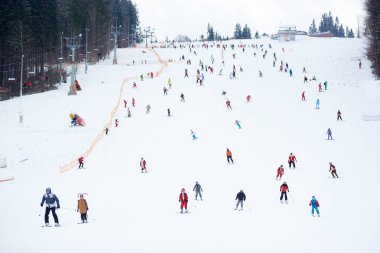 Bukovel, Ukrayna - 09 Aralık 2018: Parlak takım elbiseli kayakçılar ve snowboardcular, kablo kaldırma hattı ve kayak merkezinin yakınlarındaki geniş dağ yamacında kayak yapıyorlar. 