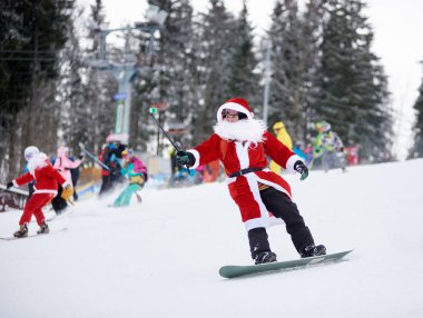 Bukovel, Ukrayna - 09 Aralık 2018: Noel Baba kostümlü snowboardcu elinde selfie monopod olan beyaz sakallı, kar kayağı yarışmasında snowboard 'a biniyor.