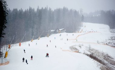 Bukovel, Ukrayna - 09 Aralık 2018: Kar yağışı sırasında Ukrayna 'nın kayak merkezindeki dağların arasında kar topu eşliğinde kayak ve snowboard yapan insanlar