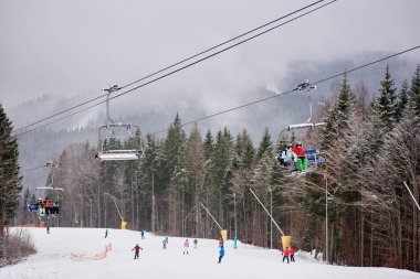 Bukovel, Ukrayna - 09 Aralık 2018: Kayakçılar ve snowboardcular, Karpatlar 'ın sisli, gri bir günde, karla kaplı yamaçlarında, kablo asansörde tek yönde oturuyorlar. 