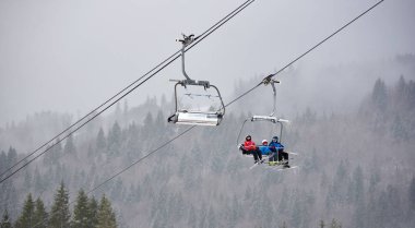 Bukovel, Ukrayna - 09 Aralık 2018: Kayakçılar ve snowboardcular, Karpatlar 'ın sisli, gri bir günde, karla kaplı yamaçlarında, kablo asansörde tek yönde oturuyorlar. 