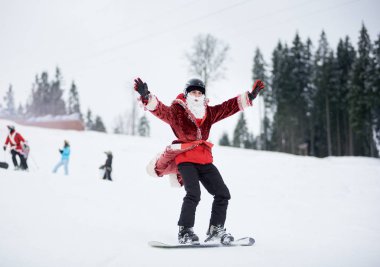 Bukovel, Ukrayna - 09 Aralık 2018: Beyaz sakallı, kar kayağı yarışmasında snowboard 'a binen Noel Baba kostümlü adam