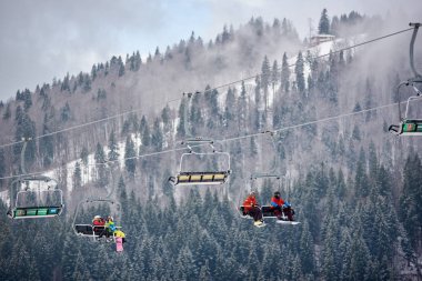 Bukovel, Ukrayna - 09 Aralık 2018: Kayakçılar ve snowboardcular, Karpatlar 'ın sisli, gri bir günde, karla kaplı yamaçlarında, kablo asansörde tek yönde oturuyorlar. 