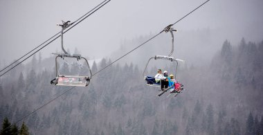 Bukovel, Ukrayna - 09 Aralık 2018: Kayakçılar ve snowboardcular, Karpatlar 'ın sisli, gri bir günde, karla kaplı yamaçlarında, kablo asansörde tek yönde oturuyorlar. 