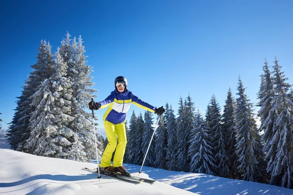 年轻快乐的女人穿着护目镜 站在滑雪板上 看着镜头 然后从雪地茂密的山下滑行 — 图库照片