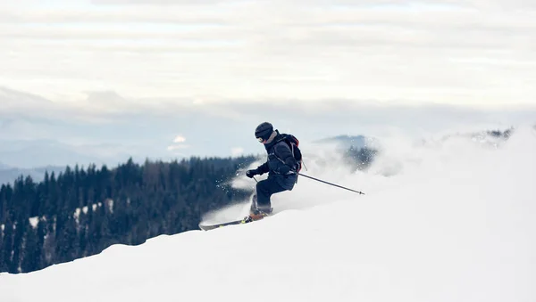 深い白い雪の粉で山から降りるフリーダースキーヤーのサイドビュー — ストック写真