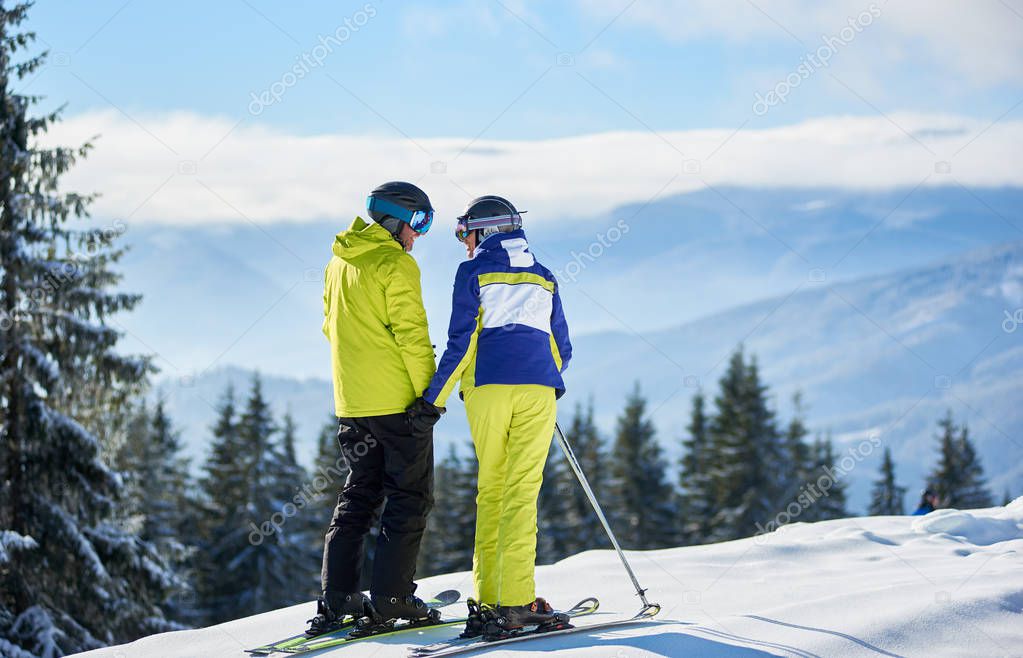 Back view of couple of skiers on mountain edge holding hands